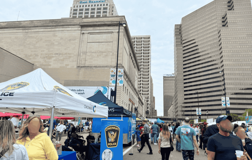 Large crowd in the City of Cincinnati during the Taste of Cincinnati 2025 featuring local police booths and downtown skyscrapers.