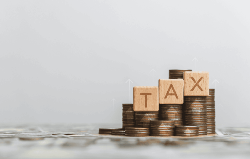Stack of coins with wooden blocks spelling TAX and an upward arrow, representing the proposed Cincinnati income tax increase for public safety funding.
