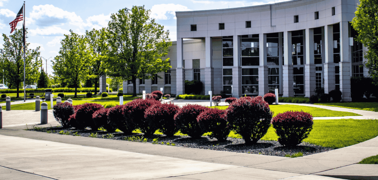 A wide-angle exterior view of the modern, white Florence Government Center building in Northern Kentucky, featuring manicured green lawns and bright red shrubs in the foreground.
