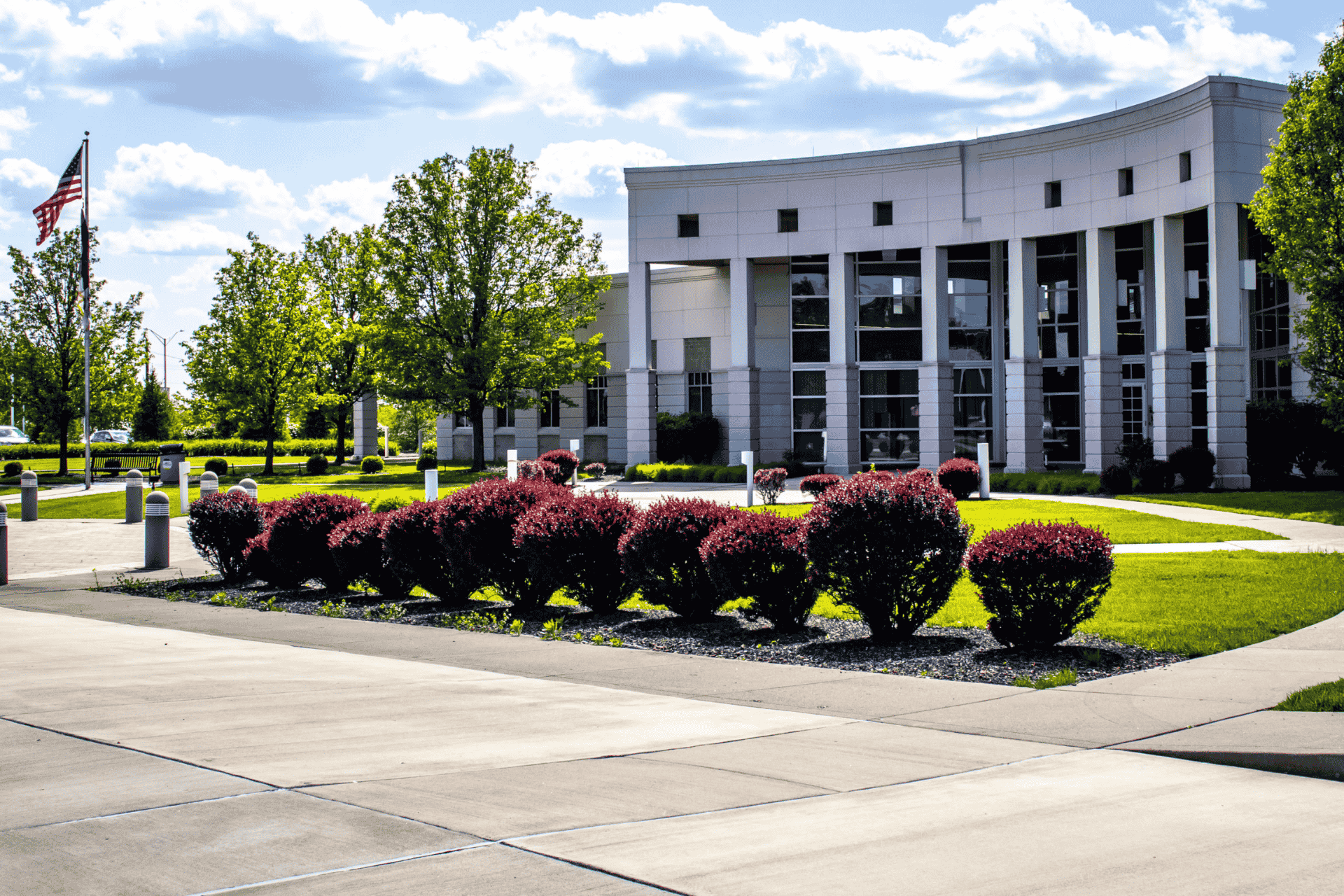 A wide-angle exterior view of the modern, white Florence Government Center building in Northern Kentucky, featuring manicured green lawns and bright red shrubs in the foreground.