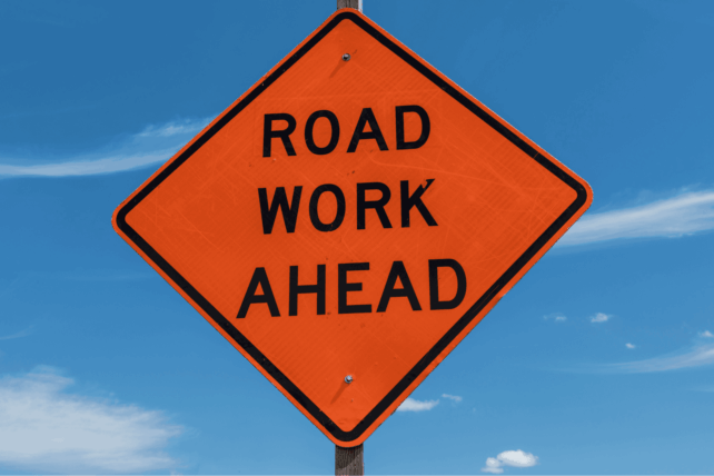 An orange diamond-shaped "Road Work Ahead" sign against a blue sky, illustrating the Fourth Street Bridge closure in Cincinnati.