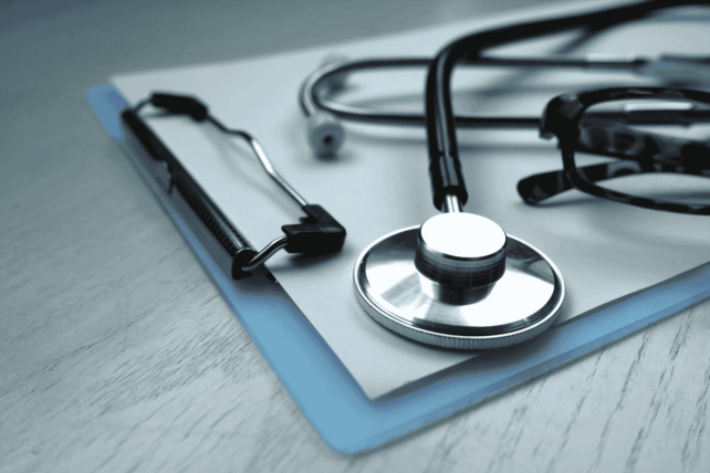A stethoscope resting on a blue clipboard on a wooden desk, representing healthcare workers Cleveland at NEON clinics.