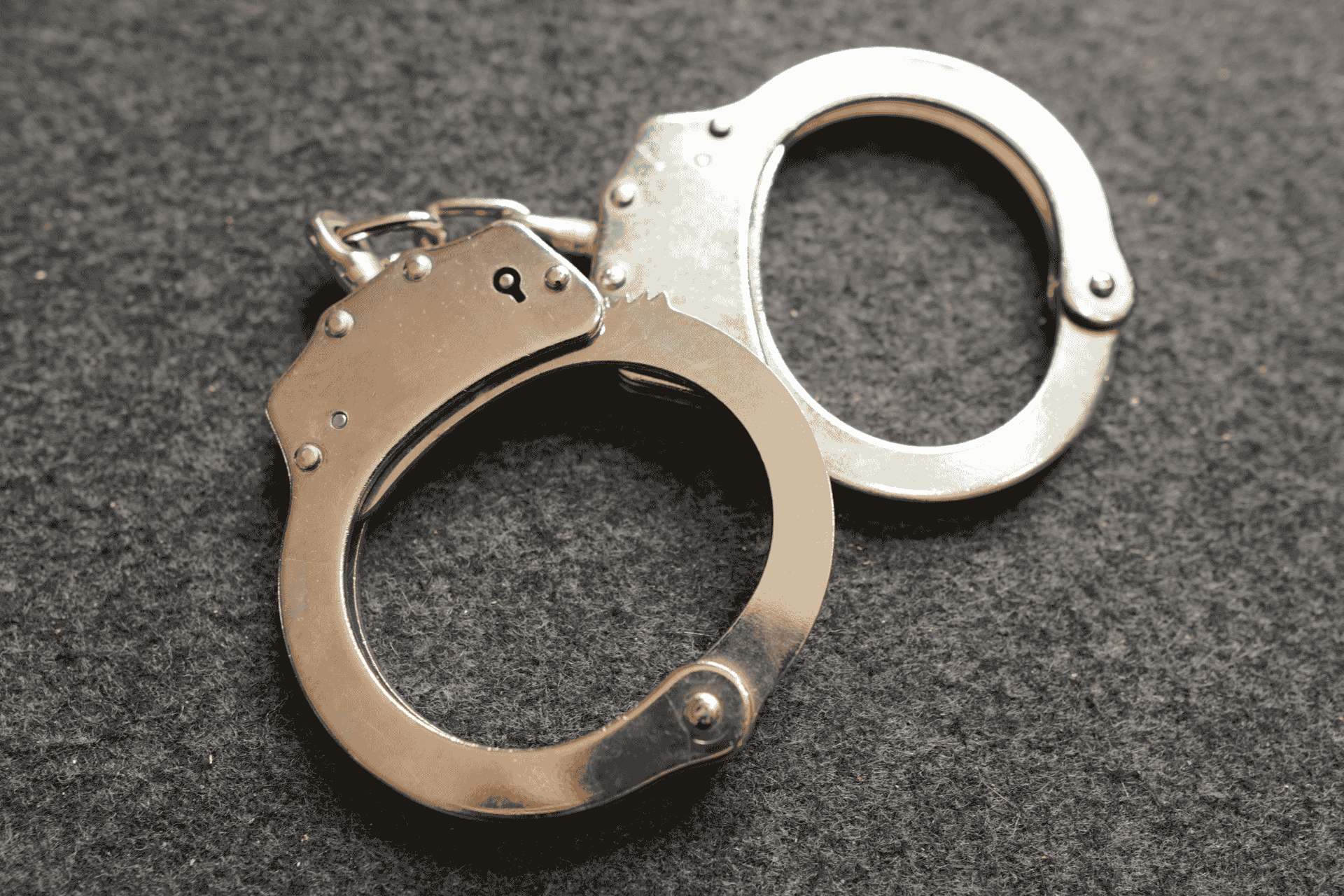 A pair of silver handcuffs lying on a dark, textured grey surface, illustrating ICE detention and law enforcement in Ohio.