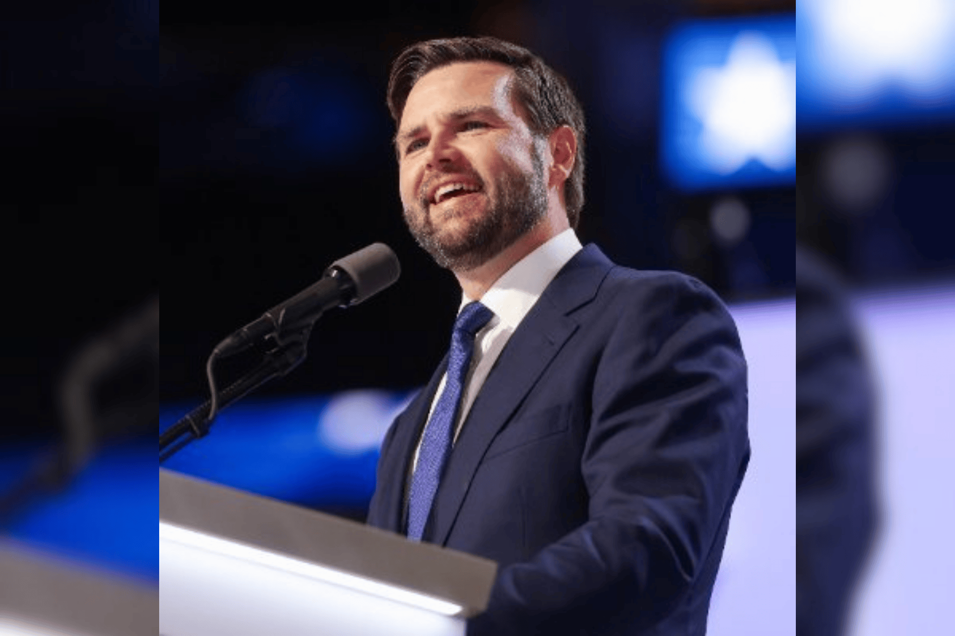 JD Vance speaking at a podium. Reports indicate windows were broken at his Cincinnati home in a vandalism incident on January 5, 2026.