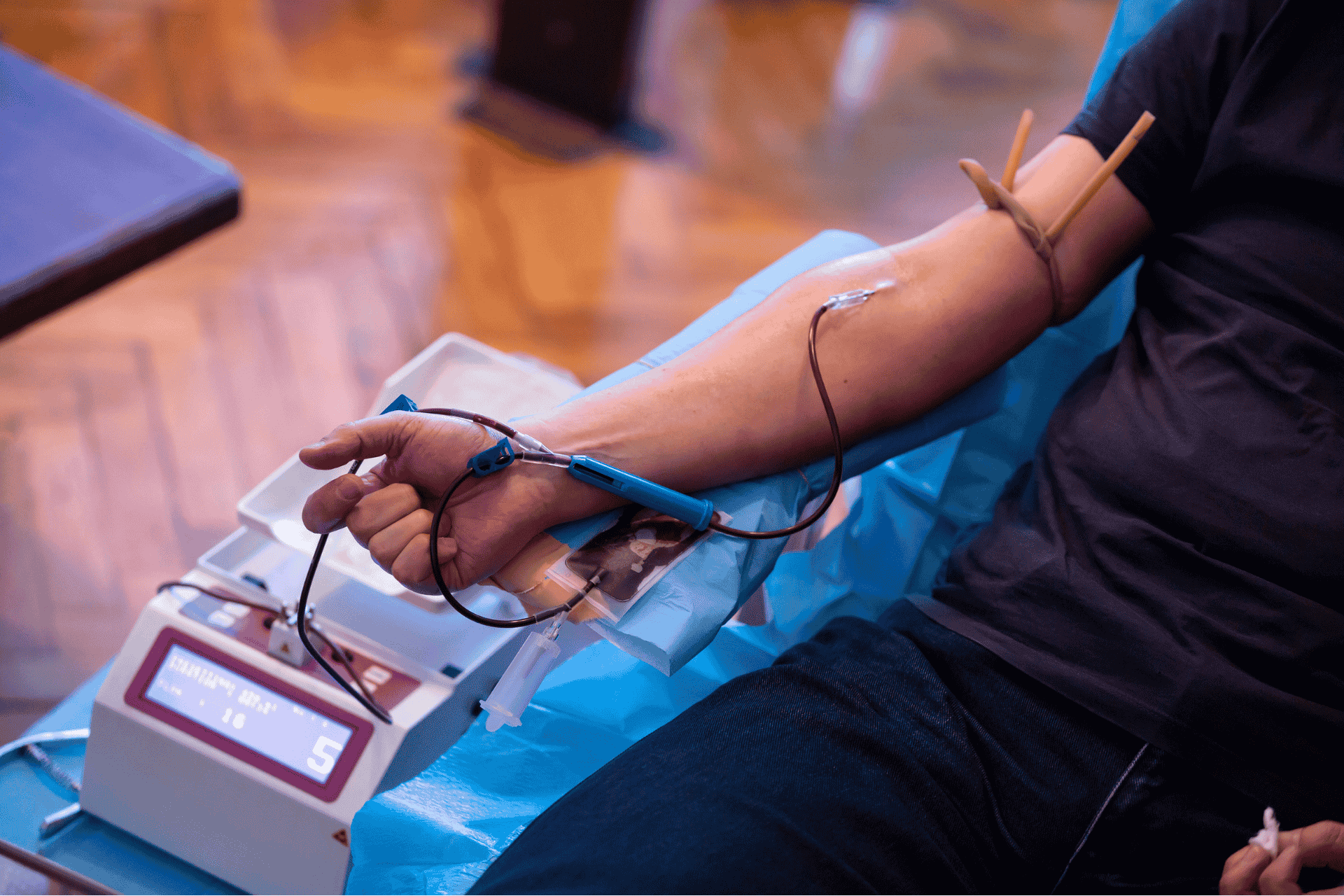 A close-up of a person's arm with a needle and tube attached during a blood donation process.