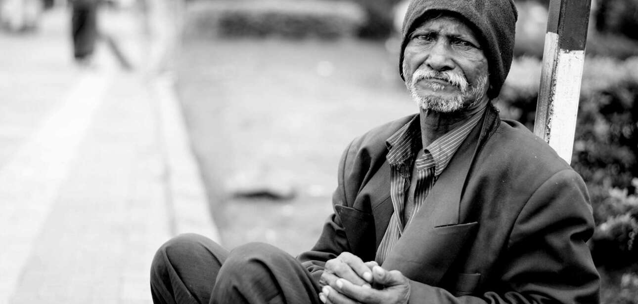 An elderly man sitting alone on a city sidewalk, illustrating urban poverty in American cities