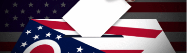 A close-up of a hand placing a white ballot paper into a ballot box, featuring a graphic of the Ohio state flag and the United States flag.
