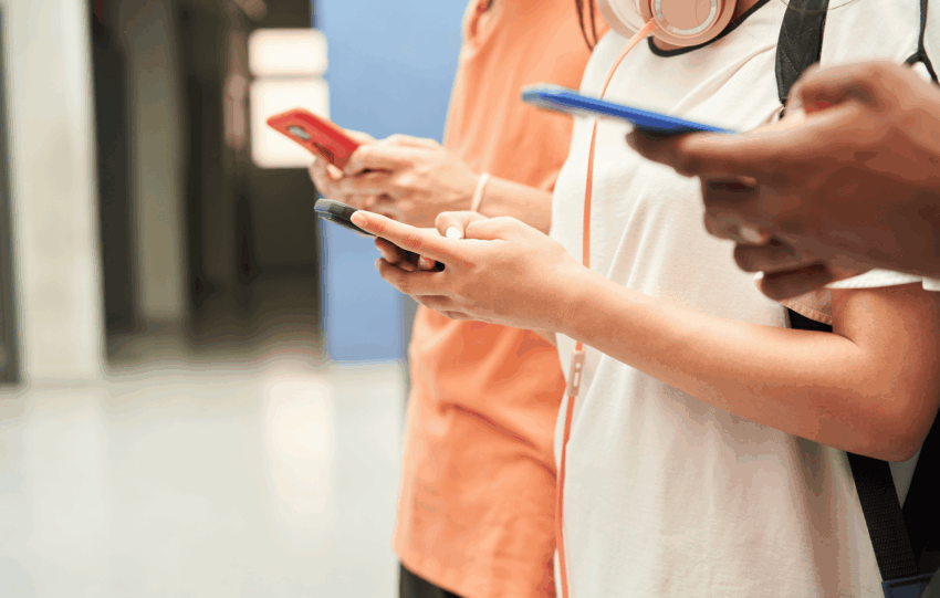 Students standing in a school hallway looking at their smartphones, illustrating the impact of the new Ohio school phone policy restrictions.