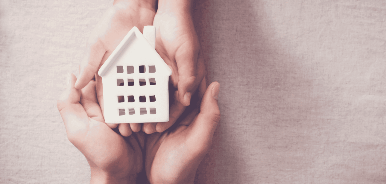 Hands holding a small white model house, symbolizing a seasonal homeless shelter in Cleveland, Ohio.