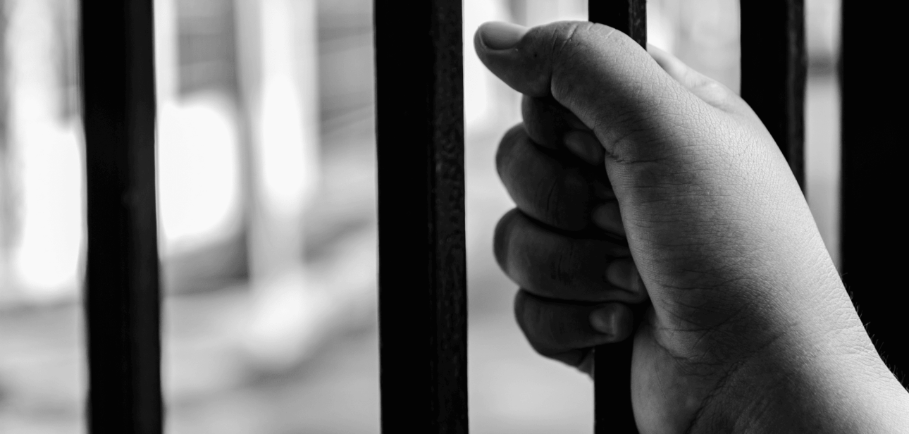 Black and white photo of a hand gripping prison bars, illustrating the indictment of a suspect in the JD Vance home vandalism case.