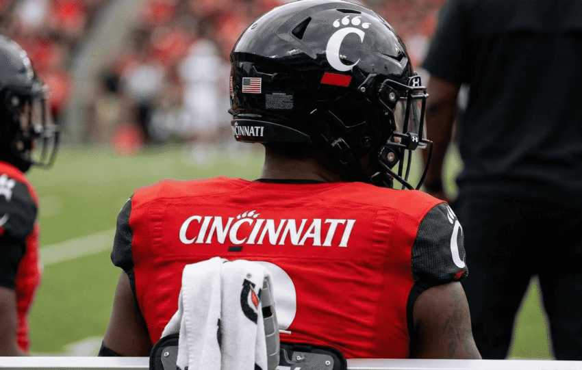 Rear view of a Cincinnati Bearcats football player wearing a red jersey and black helmet looking out onto the field.