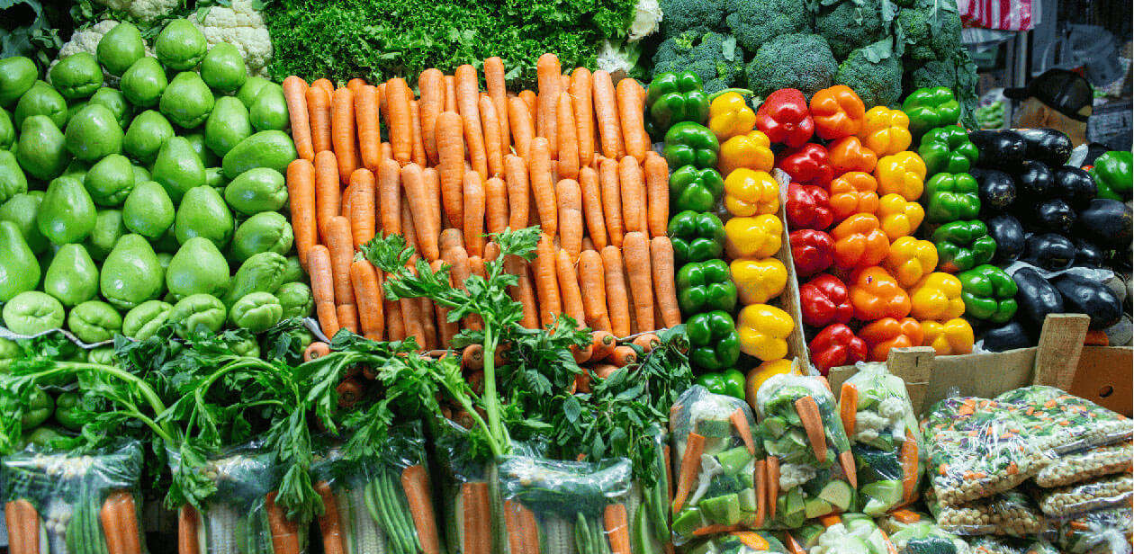 Fresh carrots, bell peppers, and leafy greens displayed in crates at a Cincinnati farmers market.