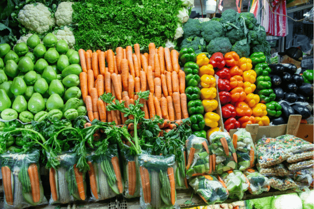 Fresh carrots, bell peppers, and leafy greens displayed in crates at a Cincinnati farmers market.