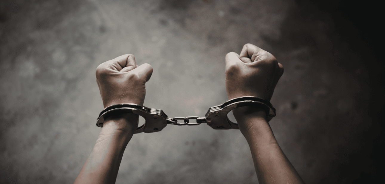 Hands of a suspect in handcuffs against a dark, textured background, representing the arrest of Willie Gordon in the Cincinnati fatal shooting case.