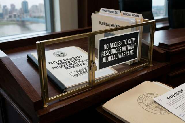 A brass-framed sign on a desk reading "No Access to City Resources Without Judicial Warrant," reflecting Cincinnati's policy limiting federal access to municipal property.
