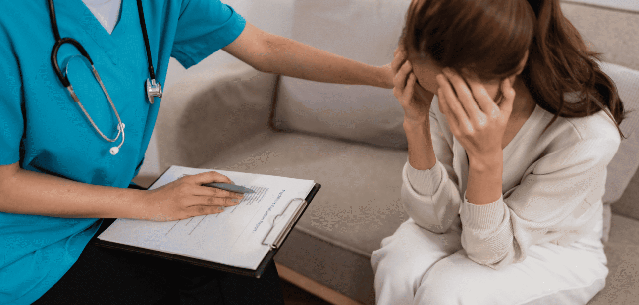 A healthcare professional in blue scrubs comforting a distressed patient during a mental health consultation.