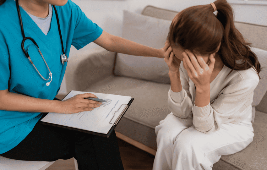 A healthcare professional in blue scrubs comforting a distressed patient during a mental health consultation.