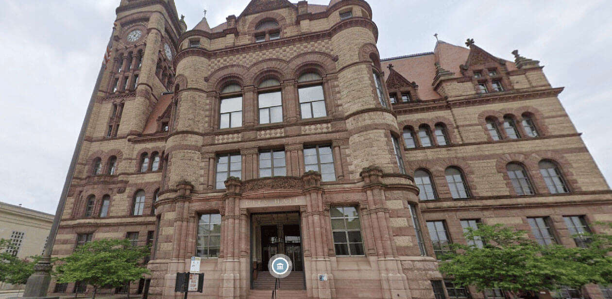 Low-angle view of the Cincinnati City Hall exterior featuring red sandstone and Richardsonian Romanesque architecture.