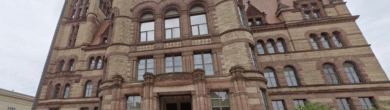 Low-angle view of the Cincinnati City Hall exterior featuring red sandstone and Richardsonian Romanesque architecture.