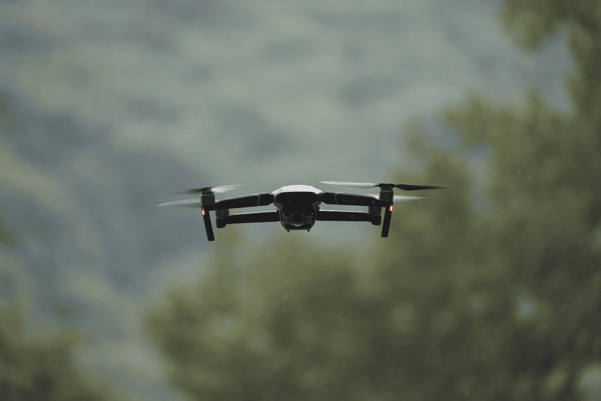 A small black quadcopter drone hovering in mid-air against a blurred background of trees and sky, illustrating defense drone production in Ohio.