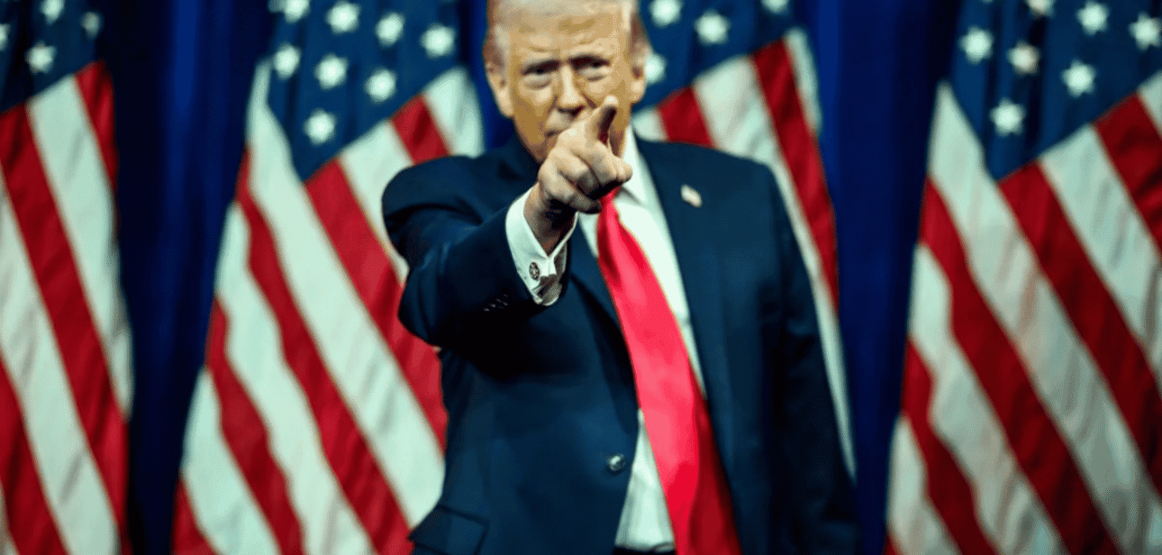 Donald Trump pointing his finger forward with American flags in the background.