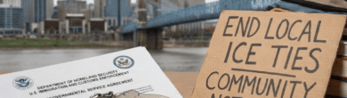 Handcuffs, an official ICE document, a toy school bus, and a cardboard protest sign reading "End Local ICE Ties, Community Not Cages" arranged in front of the downtown Cincinnati skyline and the John A. Roebling Suspension Bridge.