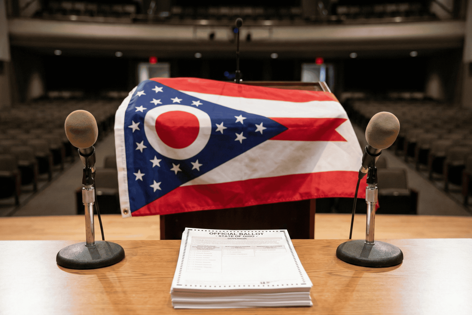 A wooden podium with microphones stands in front of the Ohio state flag, representing the open seat race for the 2026 Ohio Governor's election.