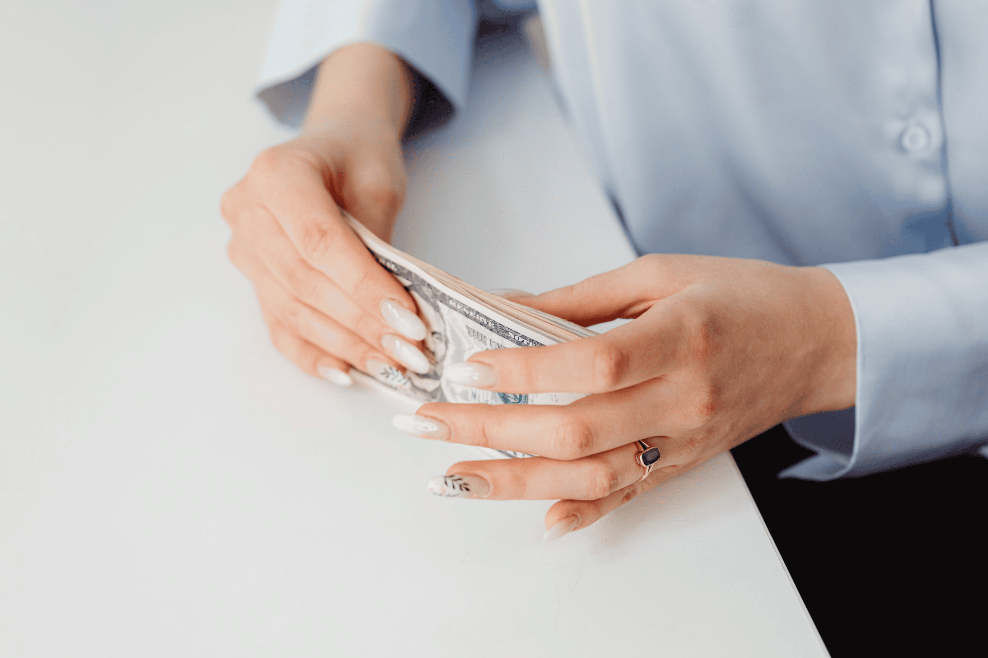 Close-up of a person's hands holding and organizing a stack of US dollar bills on a white table.