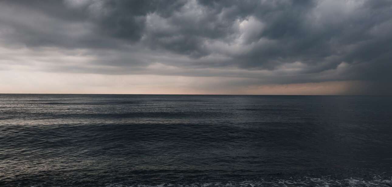 Dark, heavy storm clouds rolling in over a turbulent body of water.