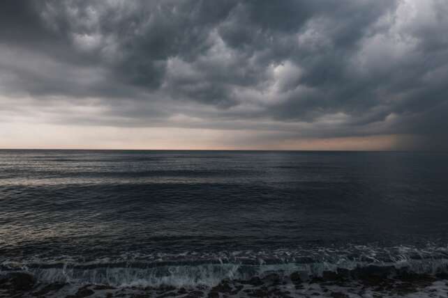 Dark, heavy storm clouds rolling in over a turbulent body of water.