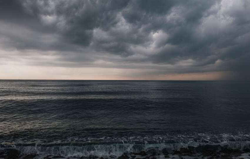Dark, heavy storm clouds rolling in over a turbulent body of water.