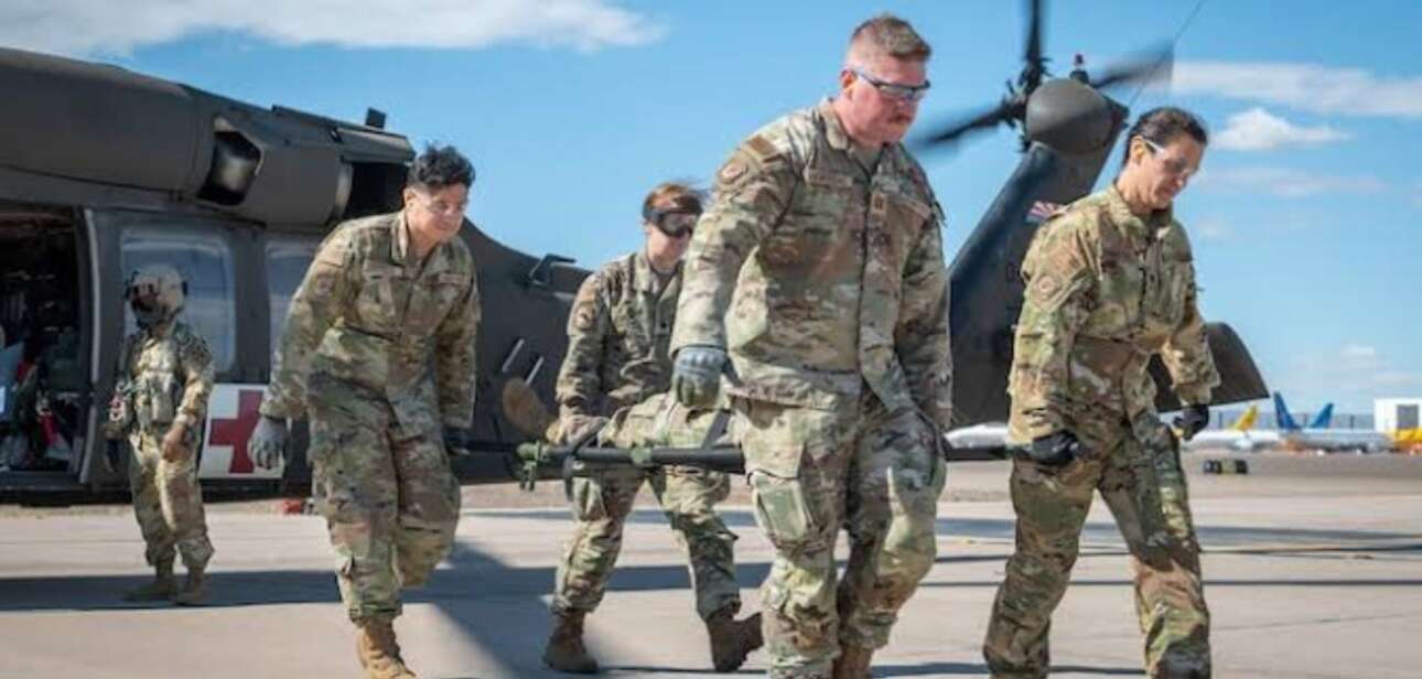 Military medical team practicing trauma patient transport with a stretcher and evacuation helicopter.