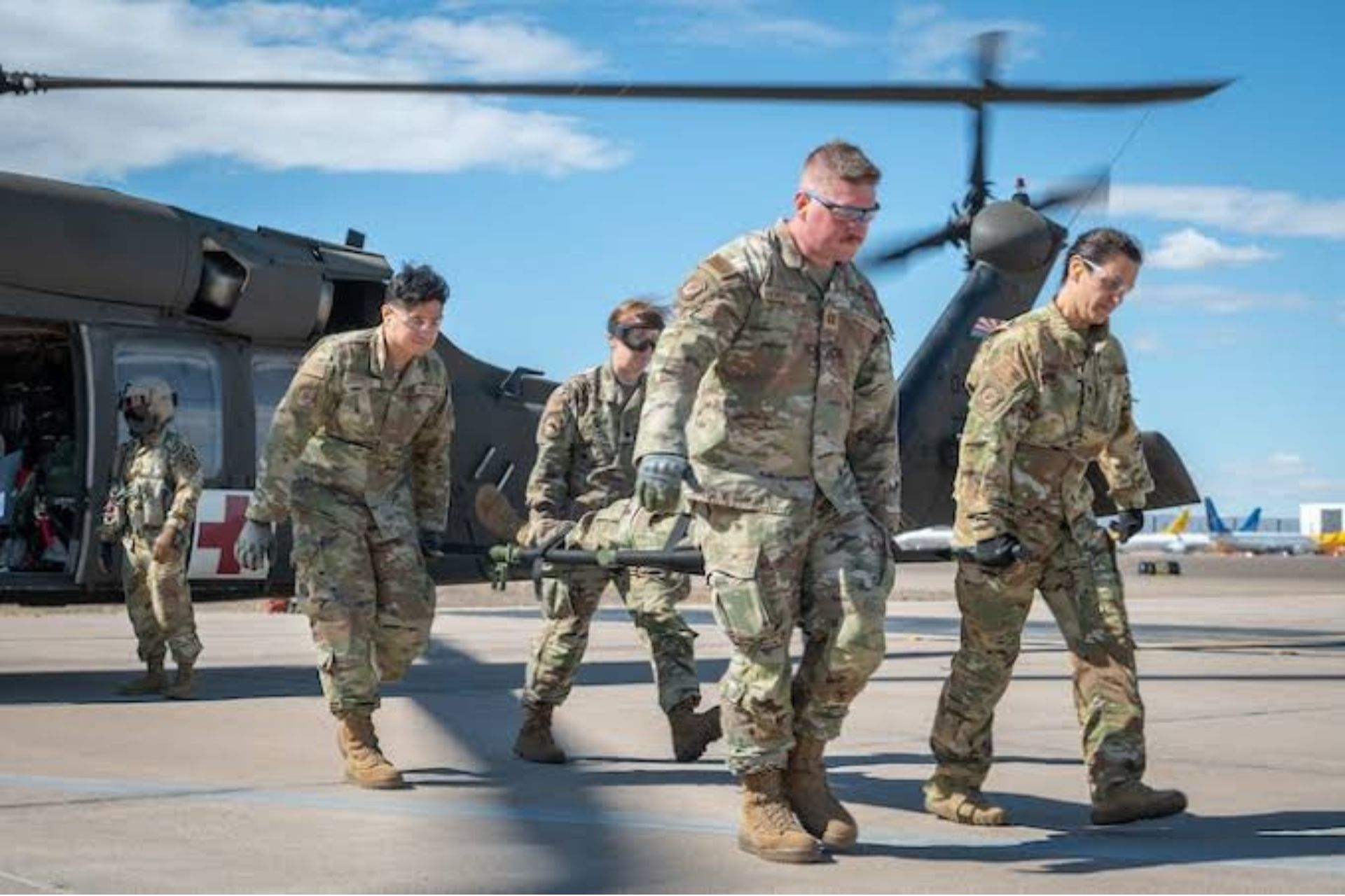 Military medical team practicing trauma patient transport with a stretcher and evacuation helicopter.