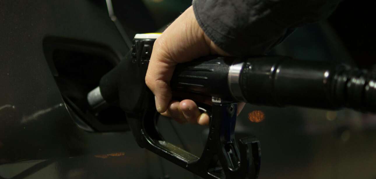 Close-up of a hand holding a black fuel nozzle pumping gas into a vehicle's tank.