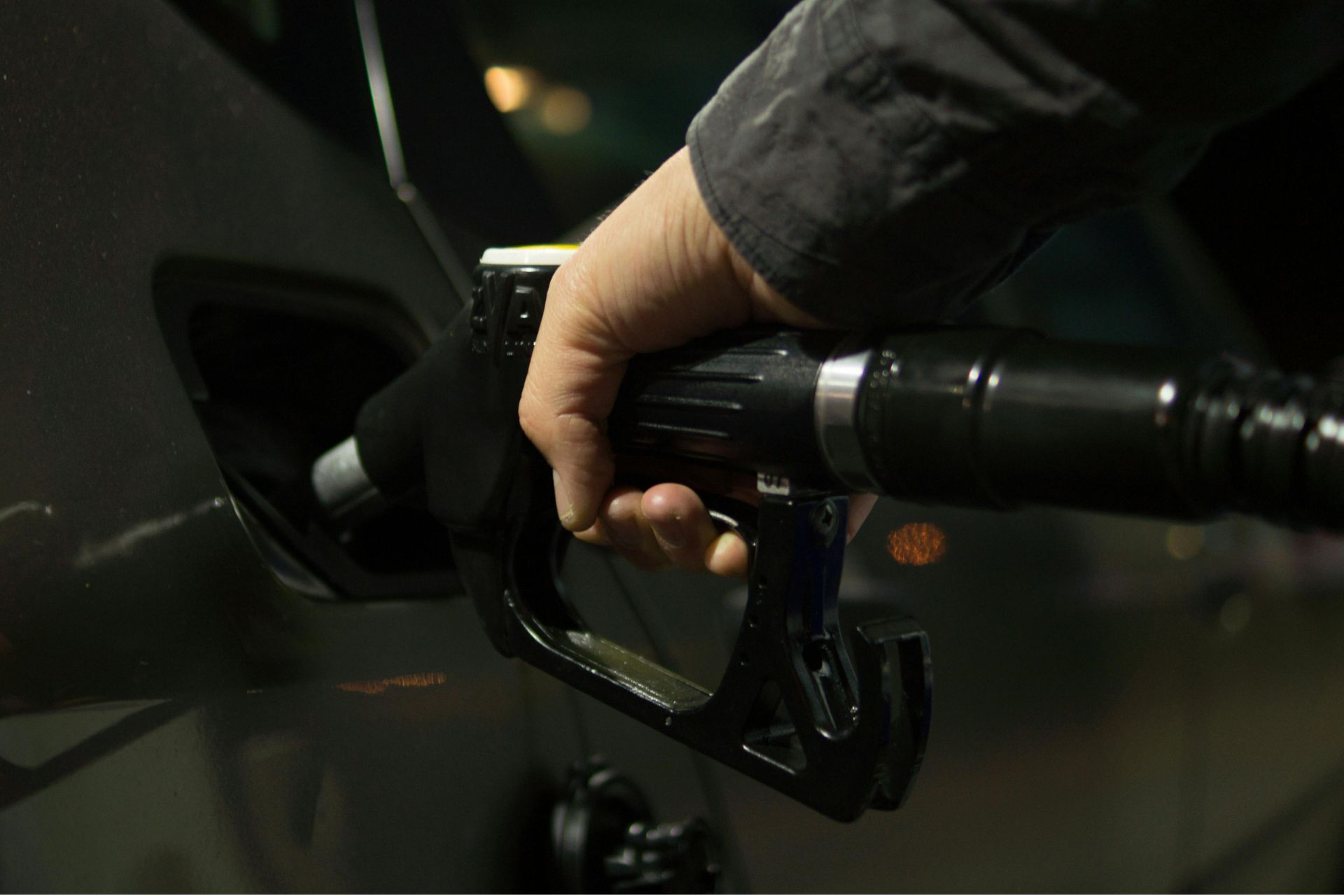 Close-up of a hand holding a black fuel nozzle pumping gas into a vehicle's tank.