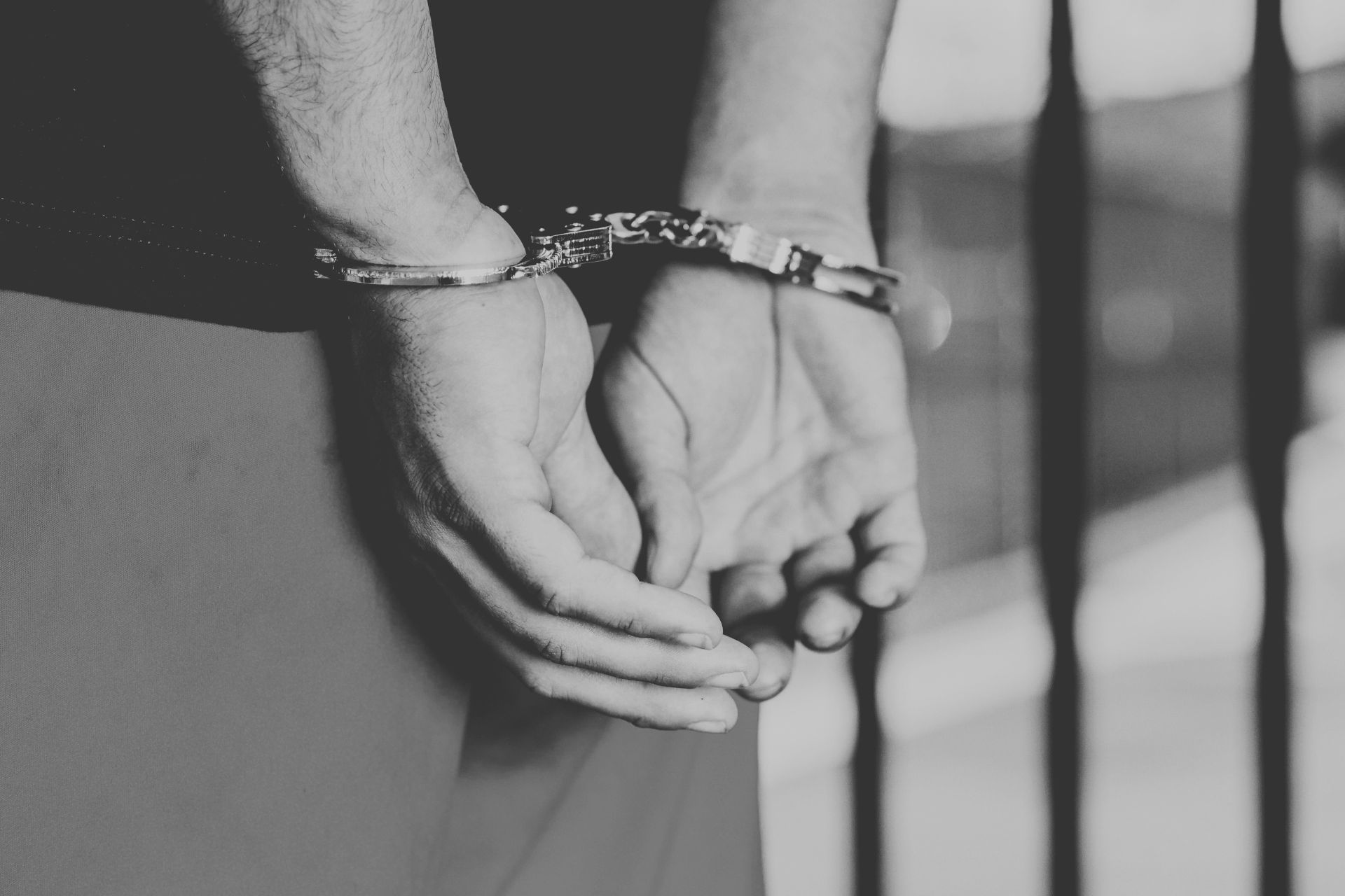 Close-up black and white photo of a person's hands in handcuffs behind their back, representing federal charges in the Cincinnati mass shooting case.