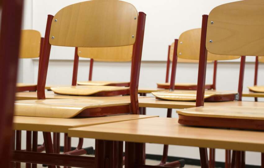 Rows of empty wooden student desks in a classroom.