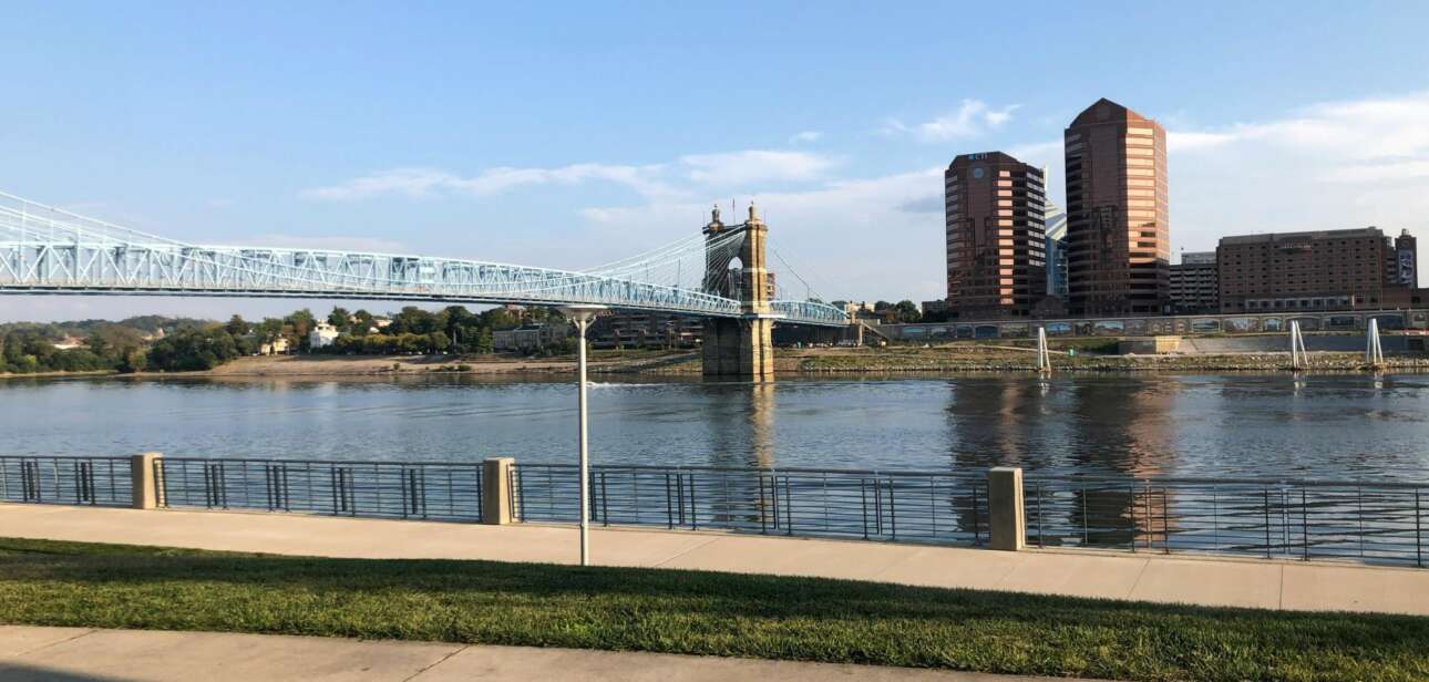 View of the John A. Roebling Suspension Bridge over the Ohio River with a news headline overlay regarding Cincinnati resident satisfaction.