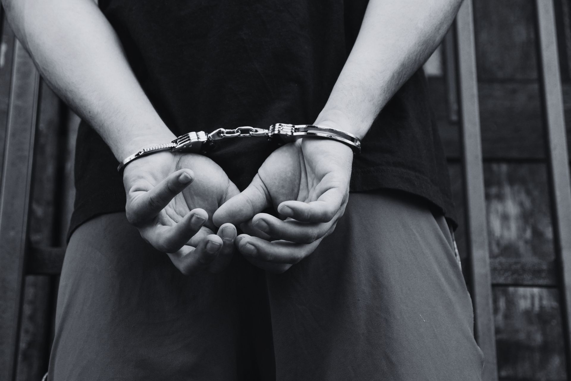 A close-up, black-and-white image of a person's hands secured in handcuffs behind their back.