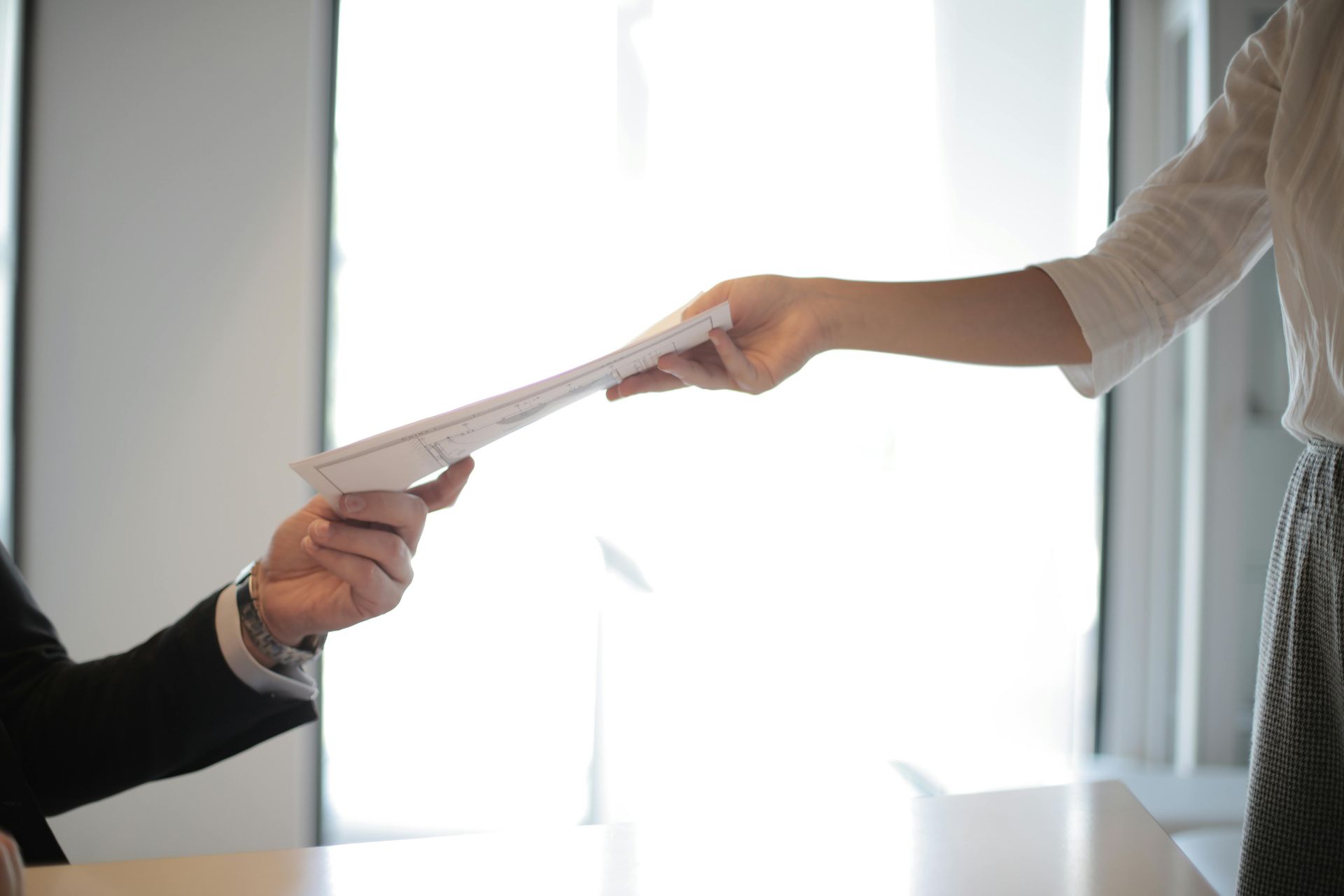 A job applicant hands a printed resume to an employer across a desk.
