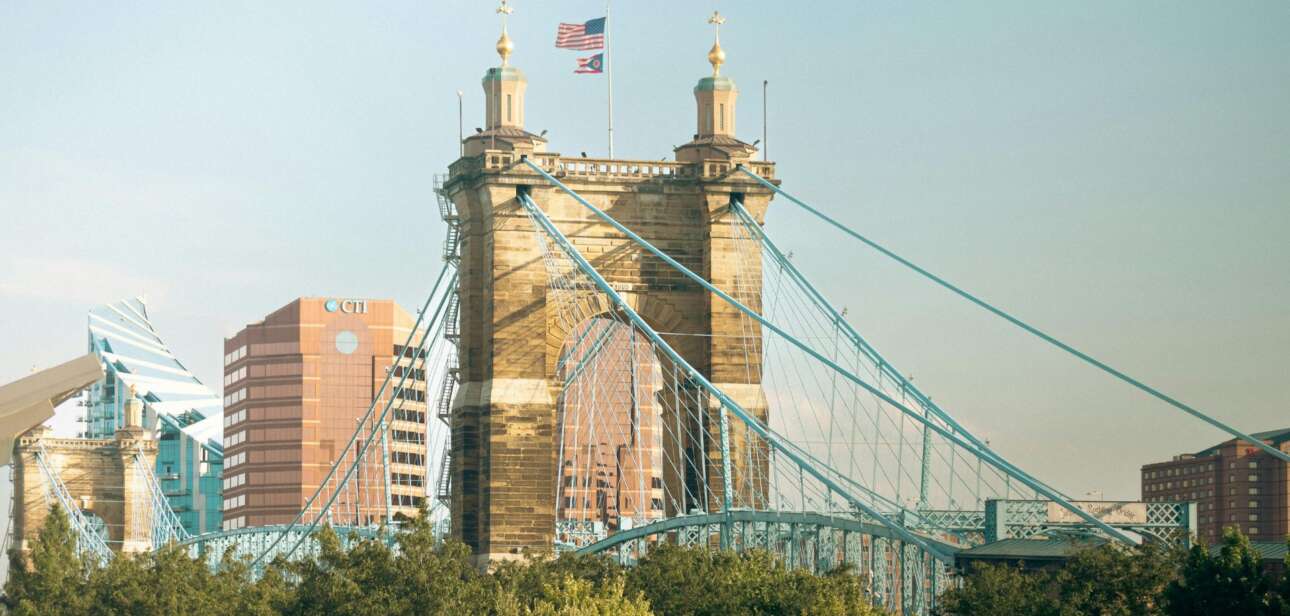 Cincinnati, Ohio skyline featuring the historic blue John A. Roebling Suspension Bridge spanning the Ohio River under a blue sky.