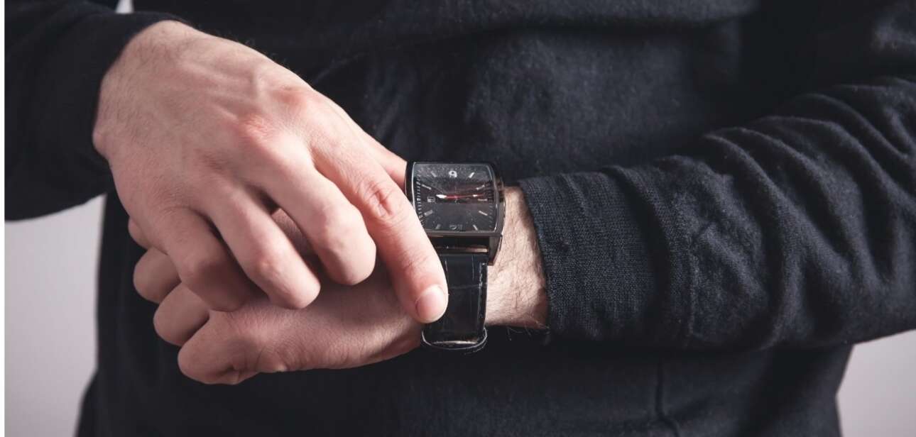 A person wearing a dark long-sleeved shirt adjusts a black luxury watch on their wrist.
