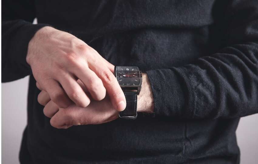 A person wearing a dark long-sleeved shirt adjusts a black luxury watch on their wrist.