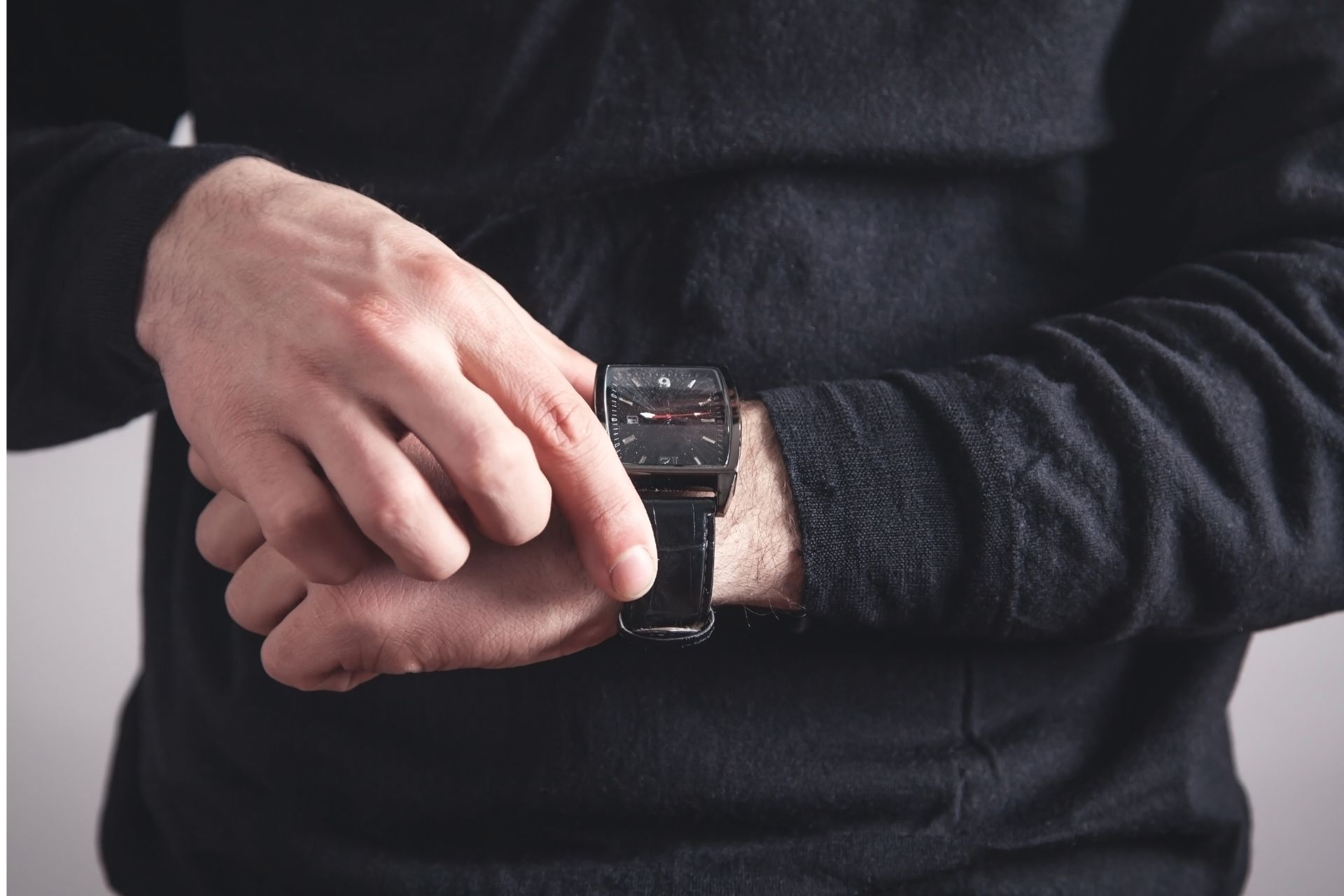 A person wearing a dark long-sleeved shirt adjusts a black luxury watch on their wrist.
