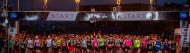 Runners gathered behind the start line banner of the Cincinnati Flying Pig Marathon in the early morning, with large ceremonial flames shooting from towers on either side of the street.