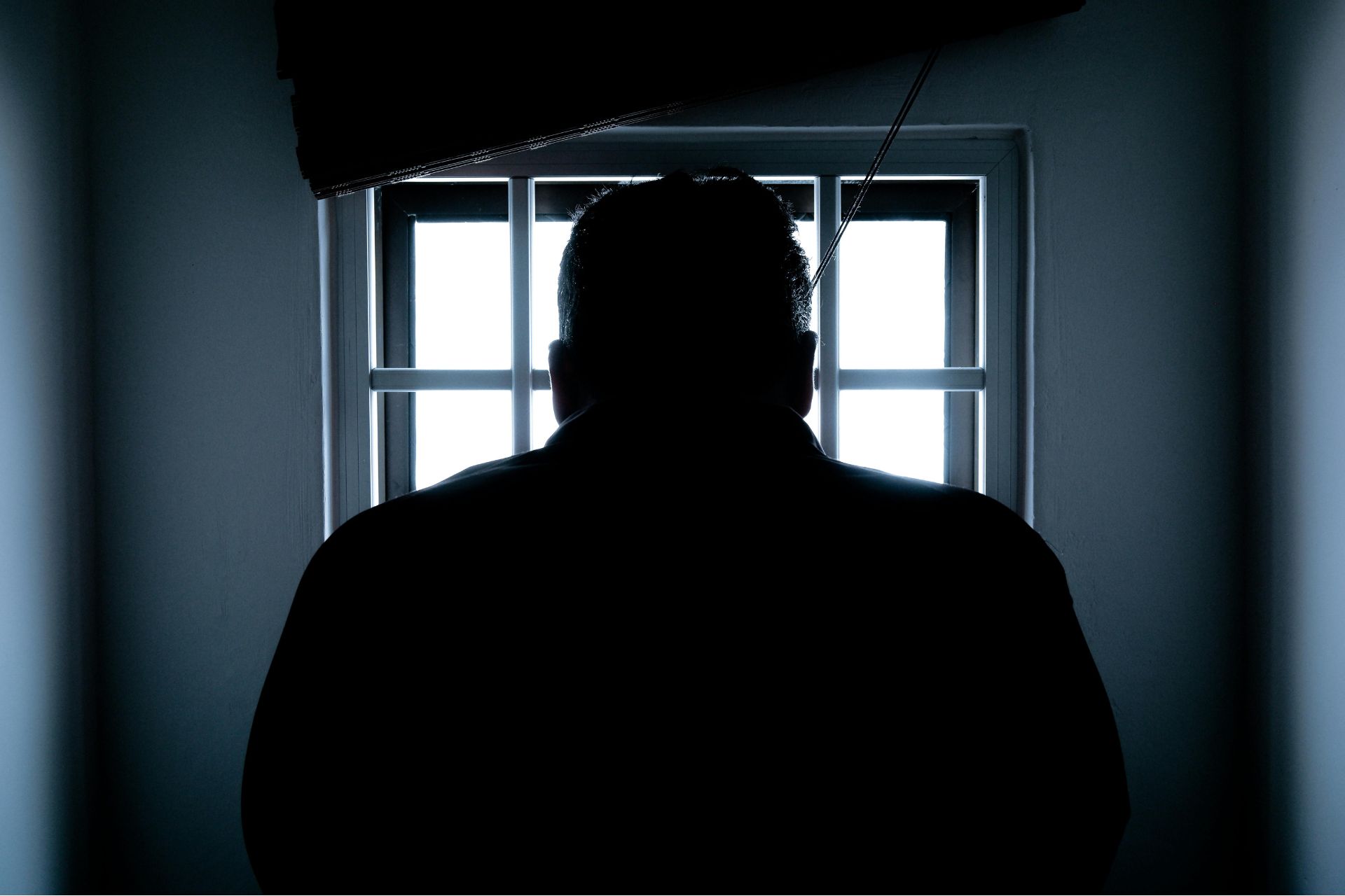 Silhouette of a person standing before a window in a dark room, illustrating a report on the Riverfront Live shooting investigation in Cincinnati.