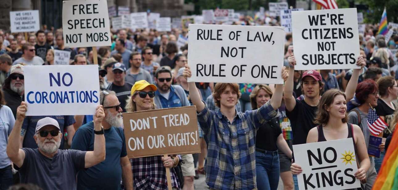 No Kings protest crowd marching with signs like “No Kings,” “Rule of Law Not Rule of One,” and “Where’s Congress” in a large city demonstration