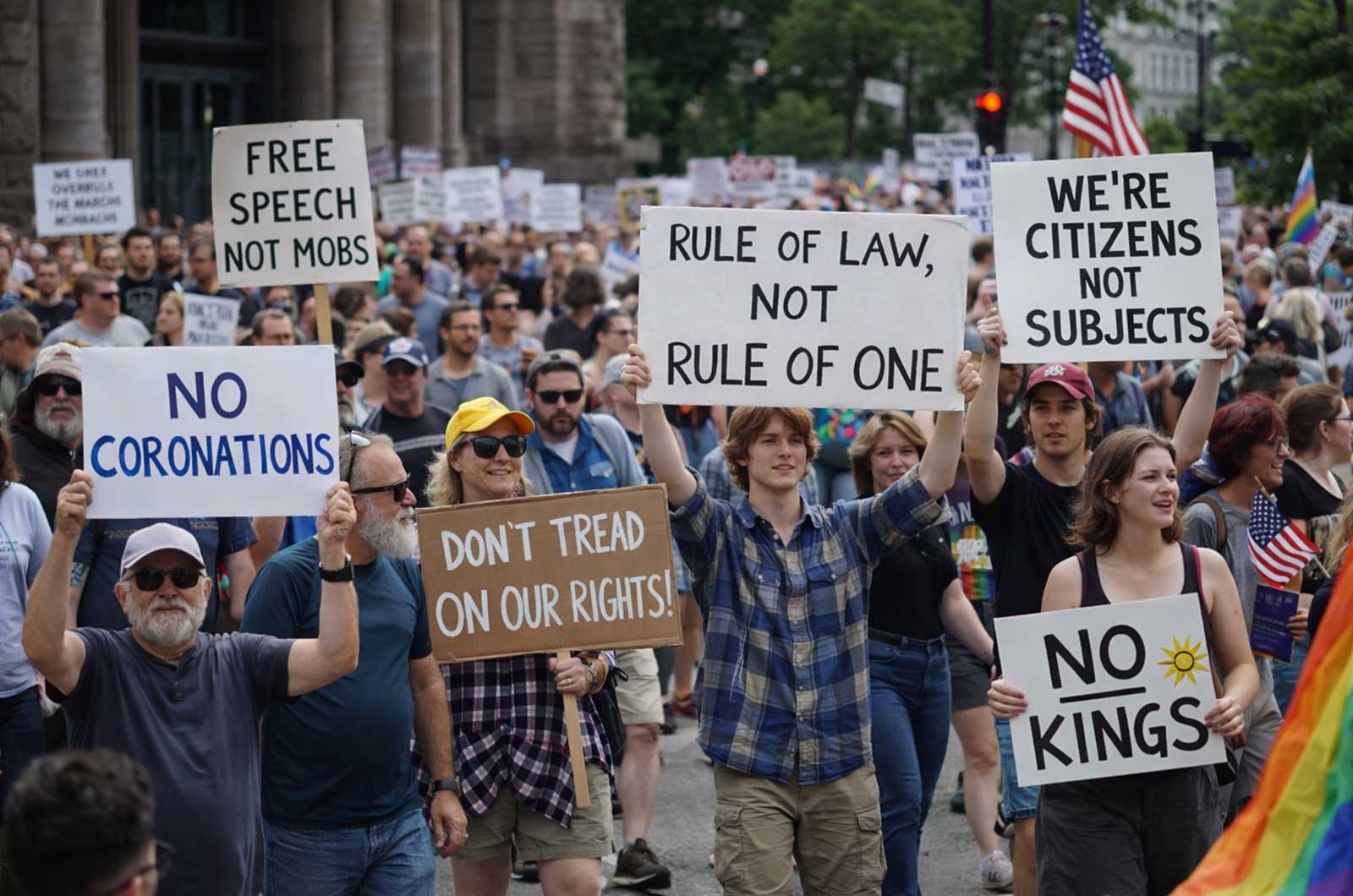 No Kings protest crowd marching with signs like “No Kings,” “Rule of Law Not Rule of One,” and “Where’s Congress” in a large city demonstration