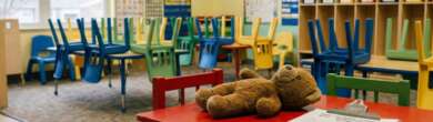 An empty daycare classroom featuring a red children's table in the foreground with a teddy bear and a clipboard of paperwork, illustrating the investigation into Ohio daycare overpayments.