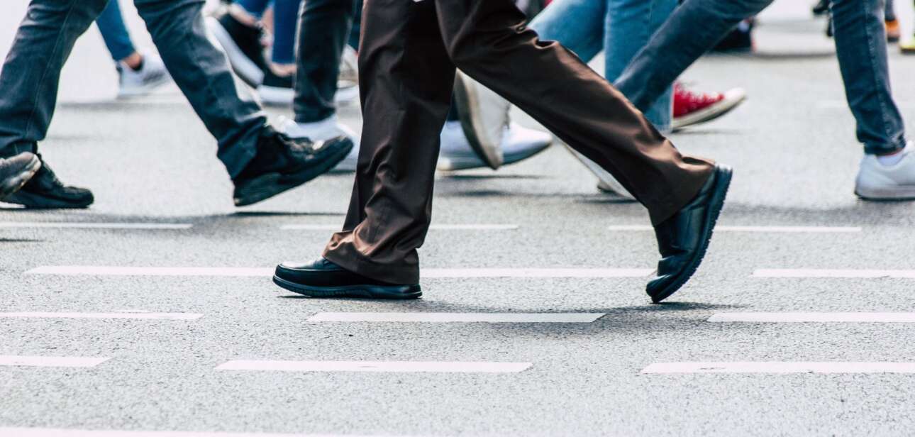 The lower half of several pedestrians walking across a painted white crosswalk on an asphalt city street.
